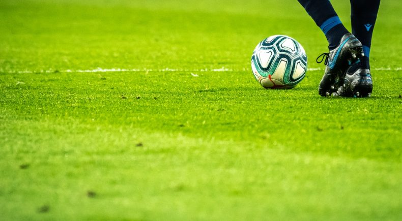 Calciatore con scarpette nere e pallone da calcio ai piedi